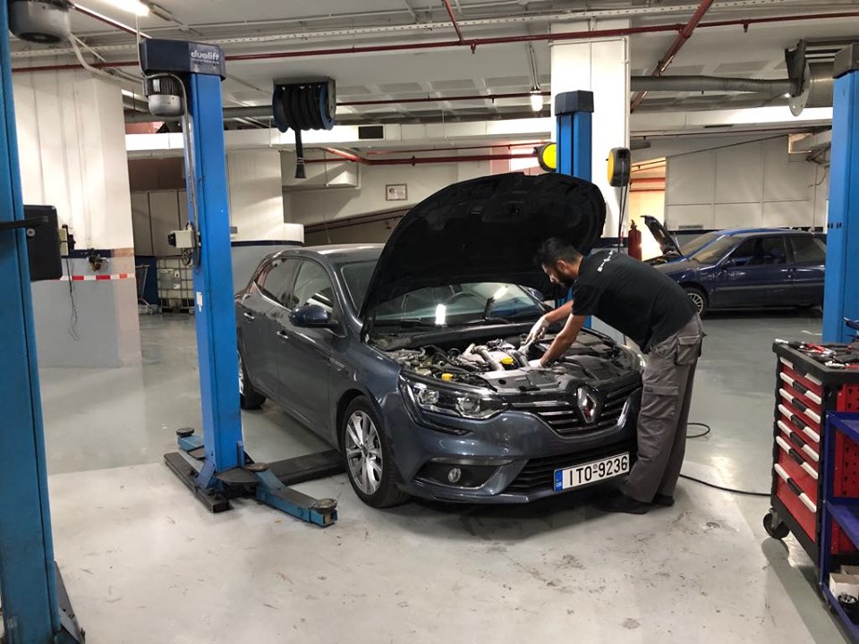 a man wearing a black t-shirt and grey pants fixing a grey car while behind him there is another car to fix