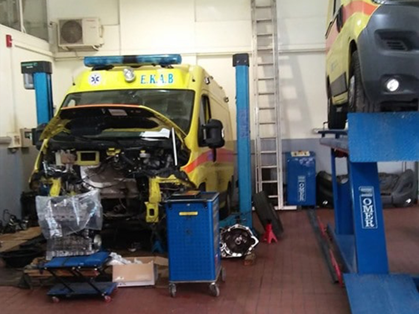 a man wearing a blue t-shirt and brown pants fixing a blue car while behind him there is another car to fix